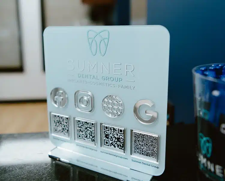 A clear acrylic countertop display featuring QR codes and the Sumner Dental Group logo.