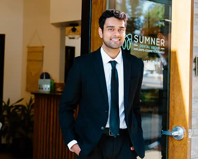 Dr. Dushyant Patel wearing a suit and tie while standing at the entrance of Sumner Dental Group.