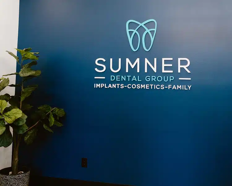 The Sumner Dental Group logo with text reading "Implants, Cosmetics, Family" on a navy blue wall.